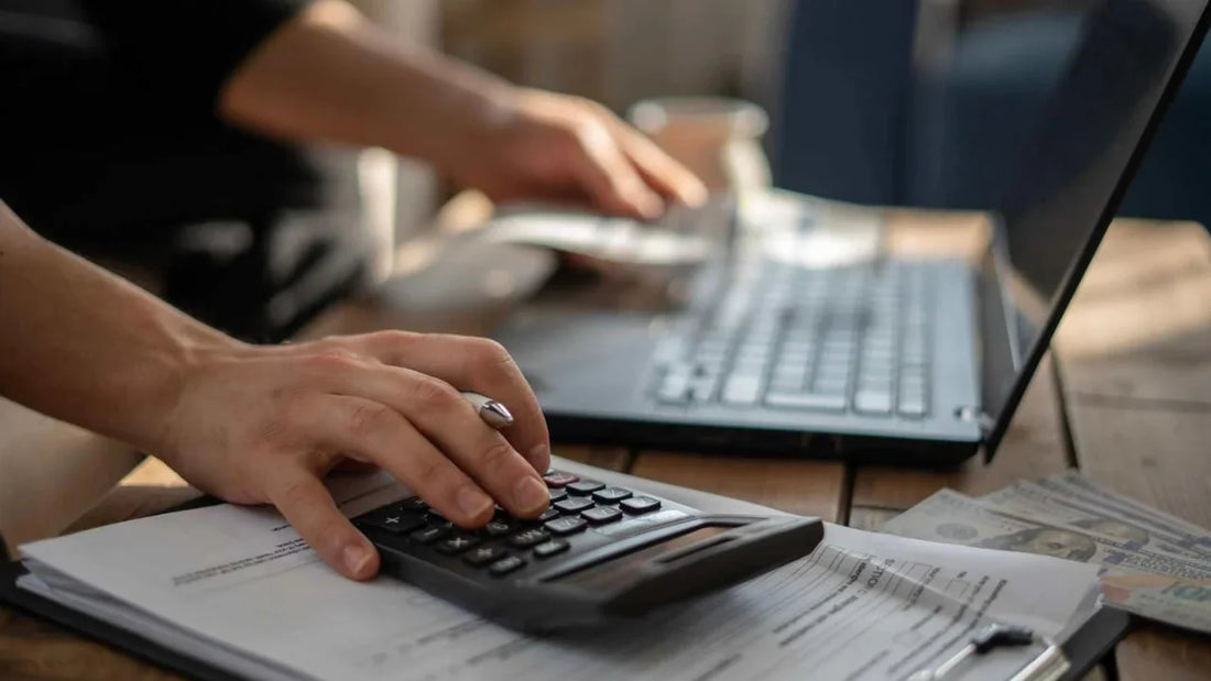 A person holding a calculator while looking at a computer