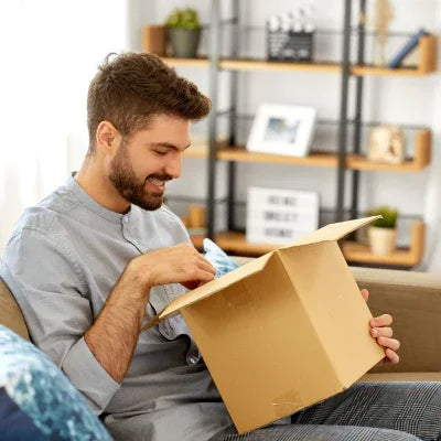 A man sitting on is couch in his living room opening a discreet box to get his CryoChoice perm Collection kit to freeze his sperm for the future.