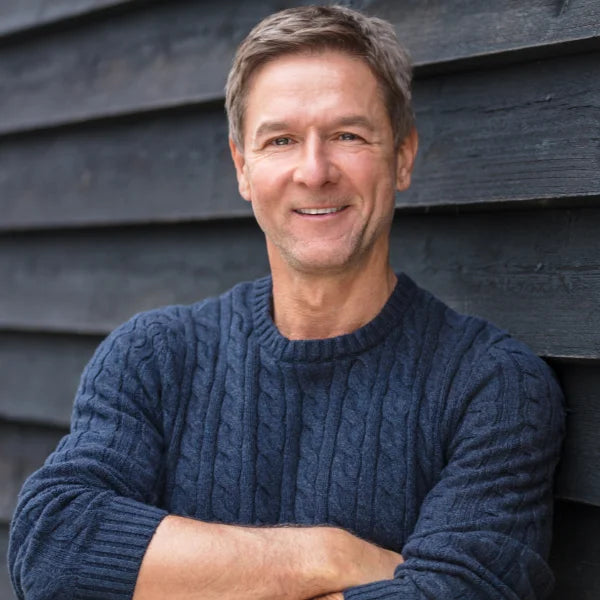 Man smiling in a blue sweater against a wall