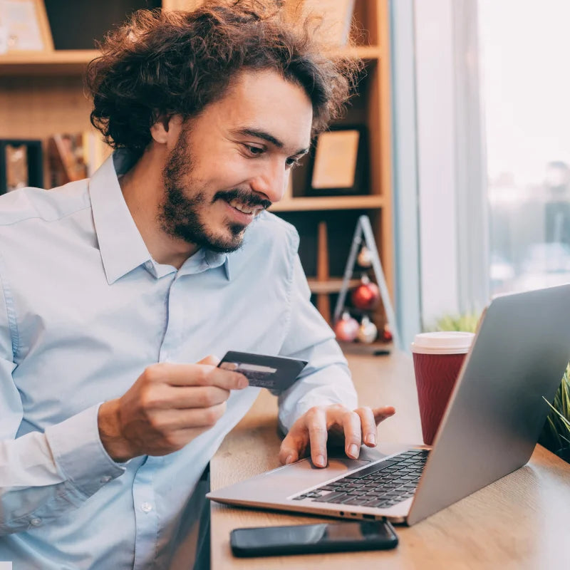 A man in a blue shirt holding a credit card looking at a laptop and making a payment on his CryoChoice account