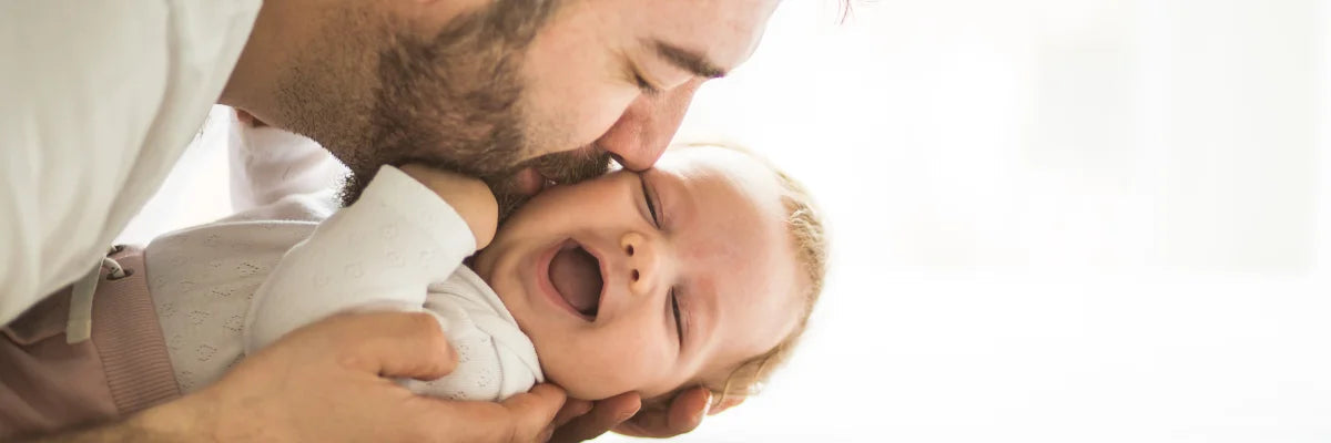 A bearded man kissing the cheek of a happy baby